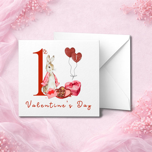Handmade baby’s first Valentine’s Day card featuring a cute bunny in pink, sitting beside heart-shaped balloons and chocolates. The text “1st Valentine’s Day” is printed in red script. Photographed flat lay with white envelope on soft pink background. Available in smooth or hammered cardstock. Perfect keepsake card for baby girl, boy, or gender-neutral celebration.