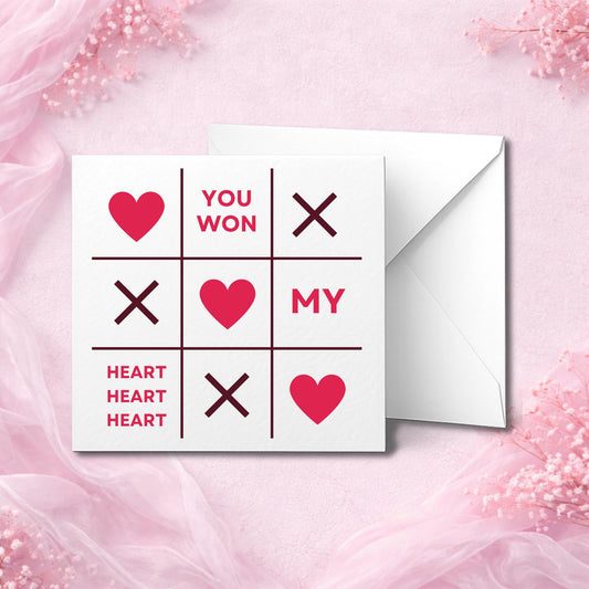 Romantic Valentine’s Day card featuring a red and pink Tic Tac Toe design with hearts and text that reads “You Won My Heart.” Printed on hammered or smooth white cardstock and shown on a soft pink chiffon background with matching envelope. Ideal luxury greeting card for couples, perfect for Valentine’s Day or anniversaries. Professionally printed with custom message option.