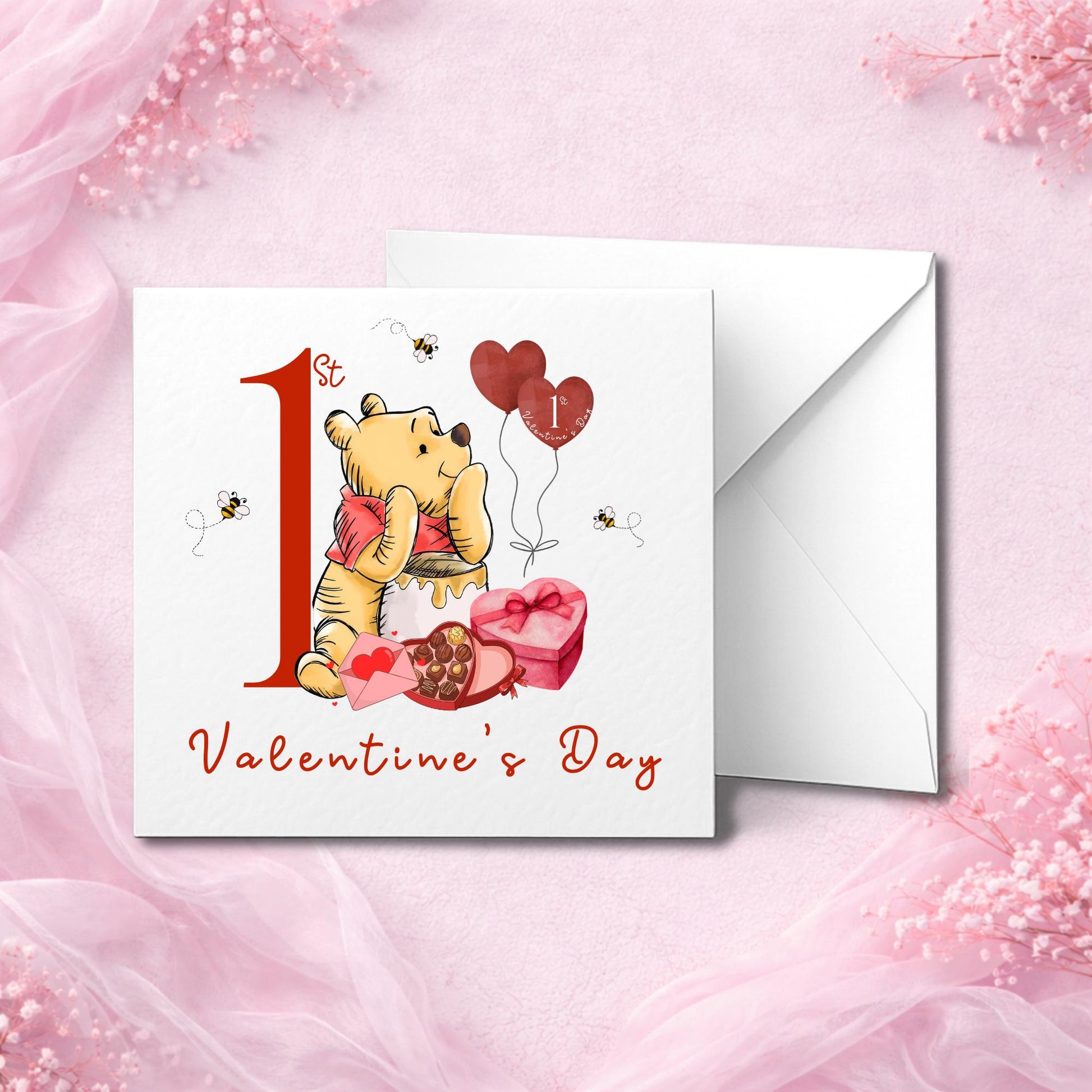 Handmade baby’s first Valentine’s Day card featuring a cuddly bear inspired by Winnie the Pooh, with honey pot, chocolates, heart balloons, and bees. Red “1st Valentine’s Day” text on white card. Paired with a crisp white envelope. Photographed on a soft pink background. Printed on premium cardstock. Great keepsake for baby girl or boy.